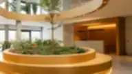 Modernus biuro vestibiulis su centrine apvalia žalumos sala ir recepcijos stalu fone.