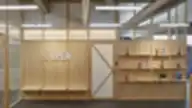 Modernus biuro interjeras su natūralaus medžio sienomis, integruotomis lentynomis, dekoratyviniais daiktais ir užrašu „We’re OPEN“.