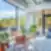 Šviesi SHED Co-living Vilnius poilsio erdvė su vazoniniais augalais ir pastelinėmis kėdėmis, dideliais langais ir išėjimu į terasą su vaizdu į mišką.