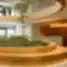 Modernus biuro vestibiulis su centrine apvalia žalumos sala ir recepcijos stalu fone.
