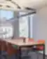Modern office meeting area with a high table, orange chairs, and pendant lights next to large windows.