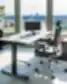 Citadele privatus biuras su reguliuojamo aukščio tamsaus medžio stalu, ergonomiška juoda tinklelio sukamoji kėde, žema juoda spintele po panoraminiais langais su vaizdu į upę ir miesto panoramą bei aukšta vazonine gyvyne.