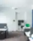 Wallter biuro dizainas, atviras ofiso planas, ergonominės žalios kėdės, balti darbo stalai, pilkos pertvaros, geltona akcentinė lempa, mėlynos užuolaidos ofise.