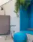 Modernus biuro poilsio kampelis su mėlynu minkštu sėdėjimo kampu, apvaliu pufu, mažais juodais staliukais ir kabančiais žaliais augalais.