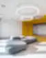 SMK moderni poilsio zona su geltonomis sienomis, apvaliais šviestuvais ir pilkais minkštais baldais.