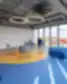 Moderni SMK kūrybinė erdvė su spalvingomis grindimis, dizaineriškomis kėdėmis ir panoraminiais langais.