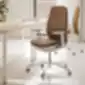 Ruda ergonominė biuro kėdė su balta baze ir ratukais prie šviesaus medinio stalo modernioje, natūralios šviesos kupinoje erdvėje.